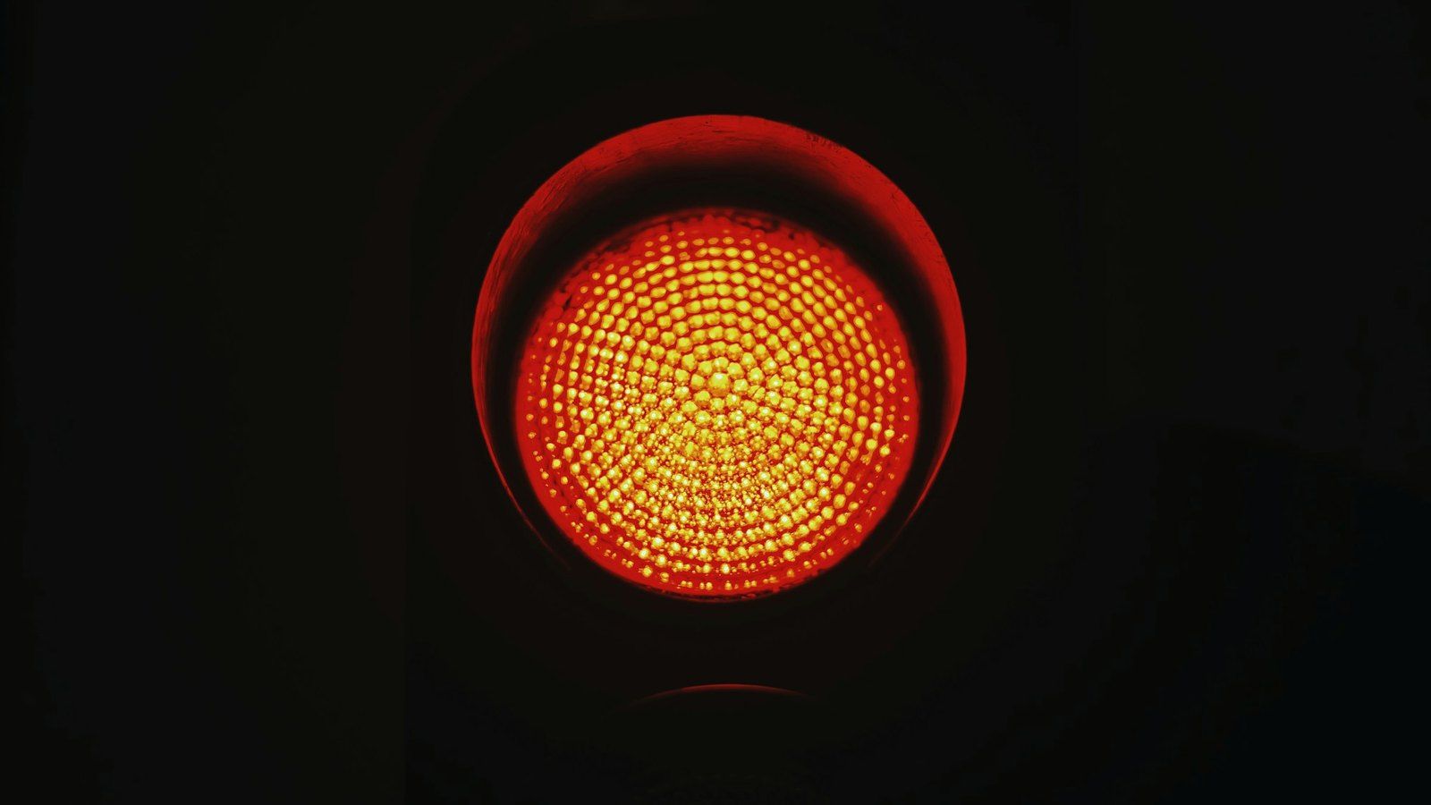 Luce rossa di un semaforo accesa, in primo piano su fondo scuro